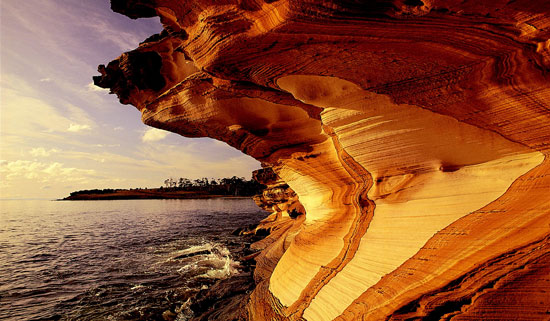 Butterscotch-colored cliffs backlit by a stormy sky on Maria’s western shoreline in Tasmania. Photo by Australia Tourism. 