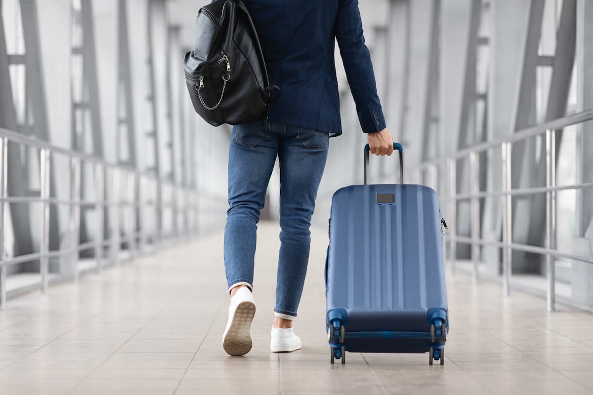 Man With Bag And Suitcase Walking In Airport Terminal. Photo by Prostock-Studio, iStock