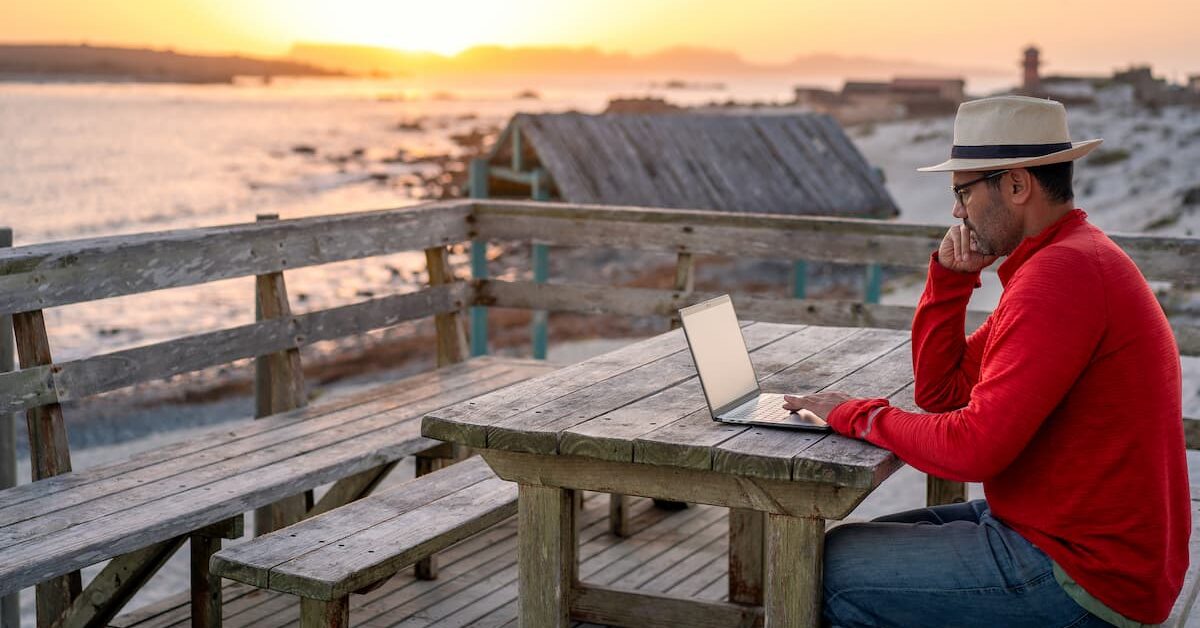 Digital nomad sitting outdoors on the beach with a laptop. Photo by Oscar Gutierrez Zozulia, iStock