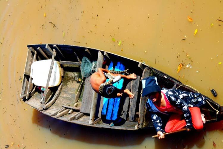 A woman in a dug-out skimmed across the lake, expecting tourists to pay to ogle at her young son who had a python draped around his neck