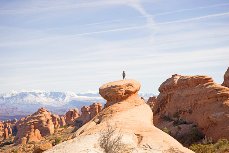 Towering a top a spiral rock formation, a man looks toward Landscape Arch in Moab, UT.