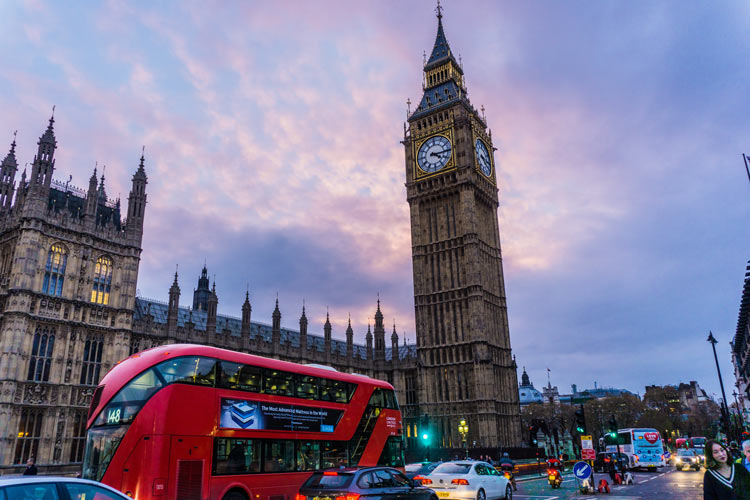 A double decker bus drives by the Big  Ben clock tower in the heart of London, UK.
