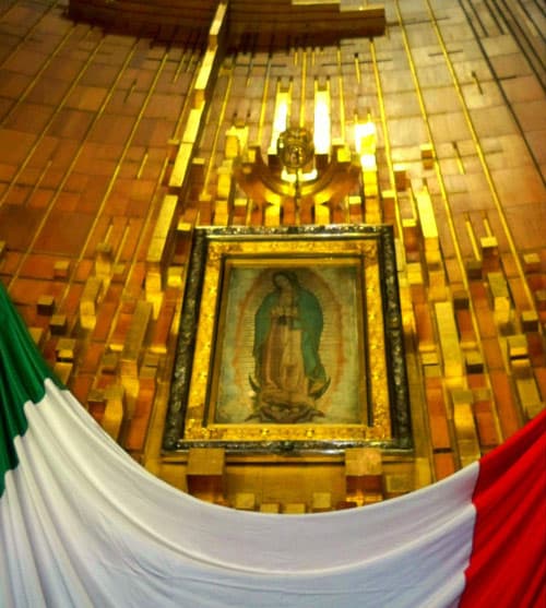 Image of the Virgin of Guadalupe hangs on a wall of gold above the Mexican flag.