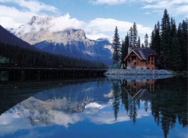 A log cabin near the lake in the mountains, reflecting the sky