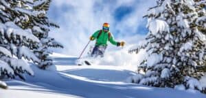 A person in a green coat and an orange helmet skis down a hill between the pine trees