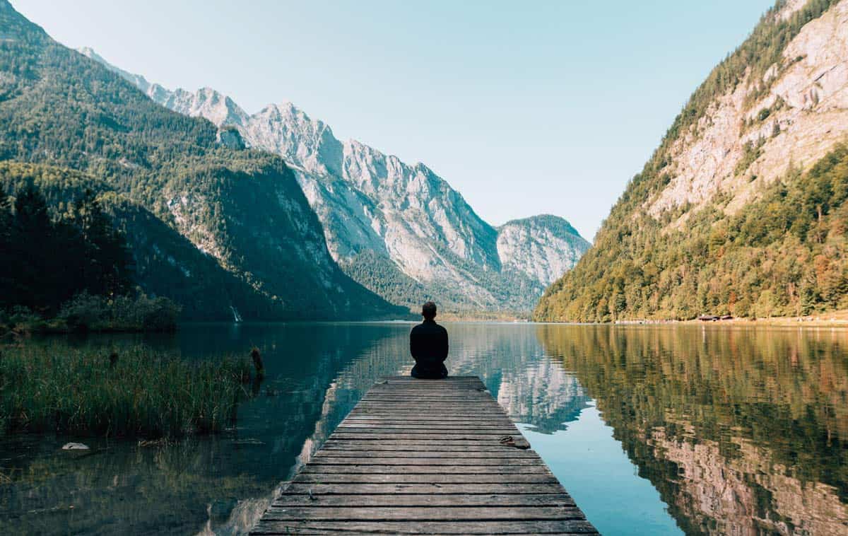 Contemplative person sitting at edge of mountain lake. Photo by Simon Migaj