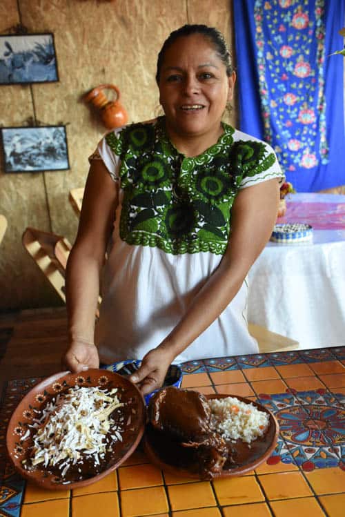 Aurelia Arroyo Martínez, owner of Jacal de Maria Calendaria, displaying enchiladas (on her right) and mole with turkey leg