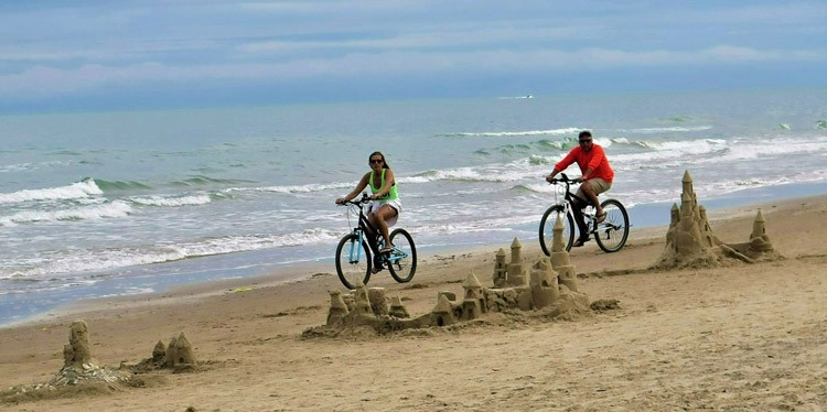 Beach bikers on South Padre Island, Texas pedaling past elaborate sand castles. Photo by Victor Block