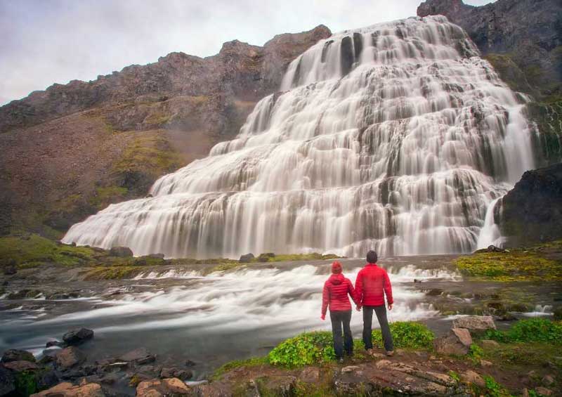 Pasangan bergandengan tangan di air terjun Dynjandi di Islandia.  Foto oleh Canva