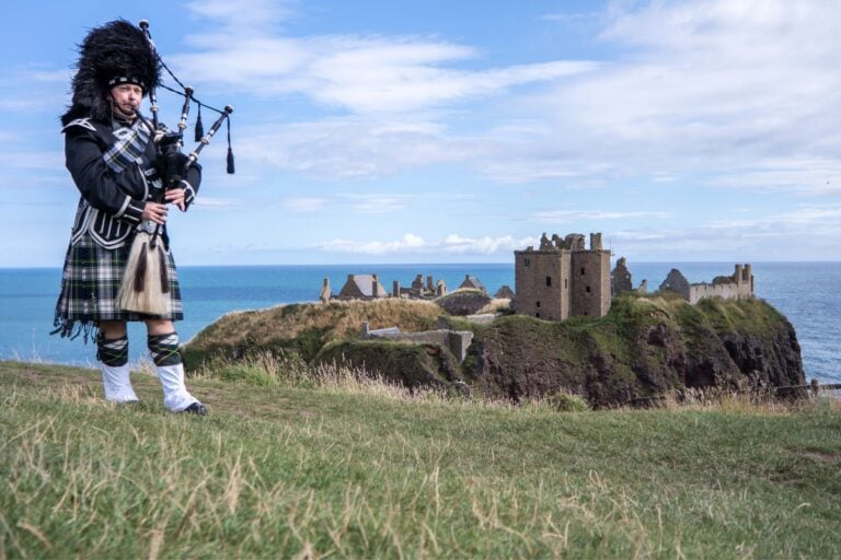 A Scottish bagpiper at one of Scotland's stunning destinations. Image by Lukassek from Getty Images via Canva