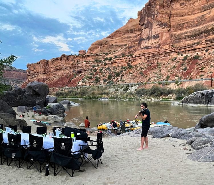 Francisco Fullana plays the violin near the dinner table at the first campsite during the Moab Music Festival’s Musical Raft Trip