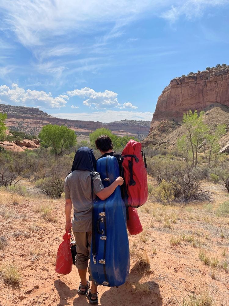 Jay Campbell and Francisco Fullana carry their instruments back to the river rafts after a concert in a natural rock setting during the Moab Music Festival