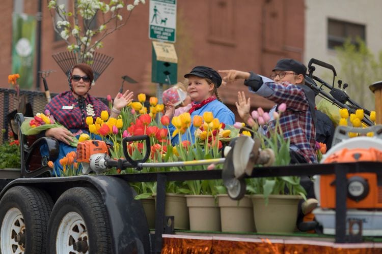 Woman and children wearing traditional dutch clothing surrounded by tulip flowers, riding a trailer at the Muziek Parade, during the Tulip Time Festival. Photo by Roberto Galan