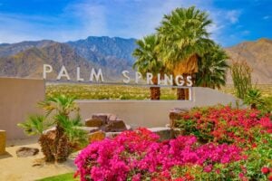 Bright bougainvillea and swaying palms frame the iconic Palm Springs sign, a perfect welcome to this desert oasis. Photo by Ron and Patty Thomas from Getty Images Signature via Canva
