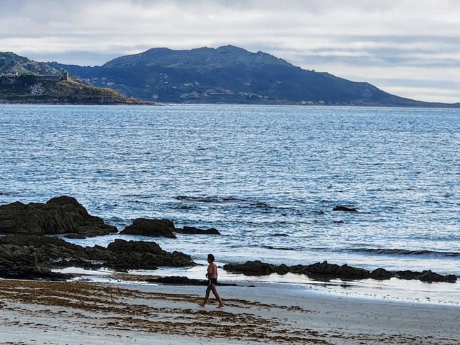 As dusk falls, a lone beachgoer walks next to the gentle surf at Praia de Panxon, Spain.