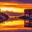 The fiery golds and oranges of Norway's midnight sun illuminate a classic Norwegian boathouse. Photo by Anders Vestin from Getty Images via Canva