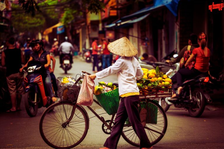 A fruit vendor cycles through Hanoi's Old Quarter, where street-side commerce pulses with the authentic energy that makes Vietnam an unforgettable destination. Image by Kamchatka via Canva
