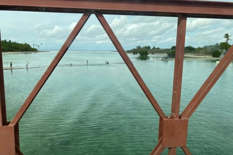 People playing on a heavy bridge for trucks next to a submerged bridge for cars at high tide.