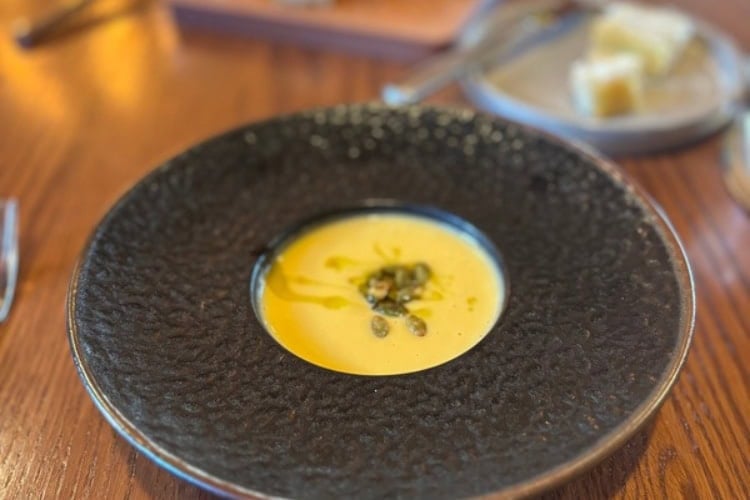 A bowl of yellow soup in a black bowl on a wooden table