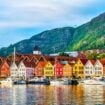 Historic Bryggen waterfront in Bergen, Norway, with its iconic colored buildings reflecting in the harbor. Photo by Elena-studio from Getty Images Pro via Canva