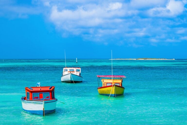 Traditional fishing boats rest in the crystalline waters off Aruba's coast. Photo by Flavio Vallenari from Getty Images Signature via Canva