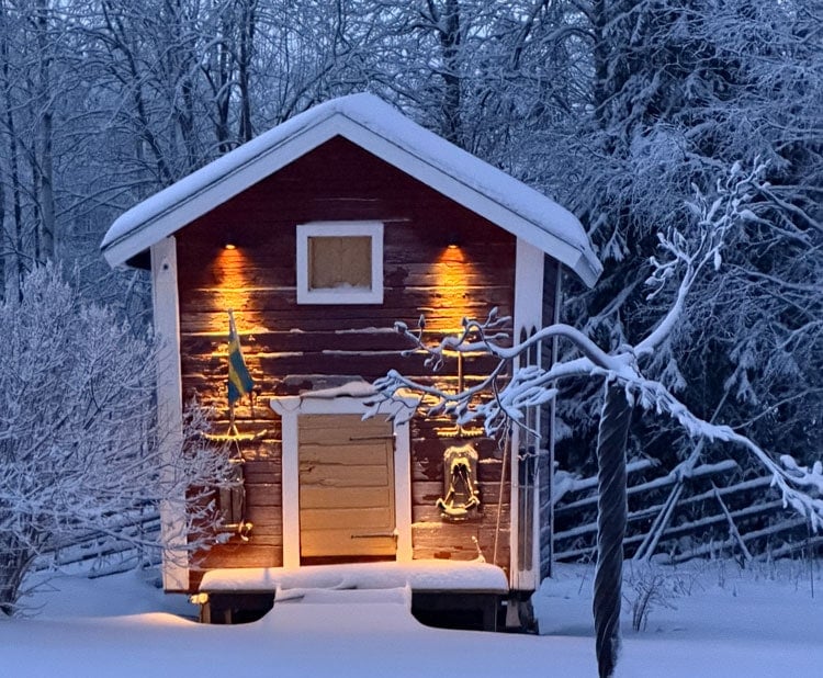 A charming snowy cabin in winter forest with warm exterior lighting. Perfect travel destination for winter adventures.
