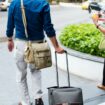 A traveler with two bags walks on a sidewalk. Photo by Curated Lifestyle, Unsplash