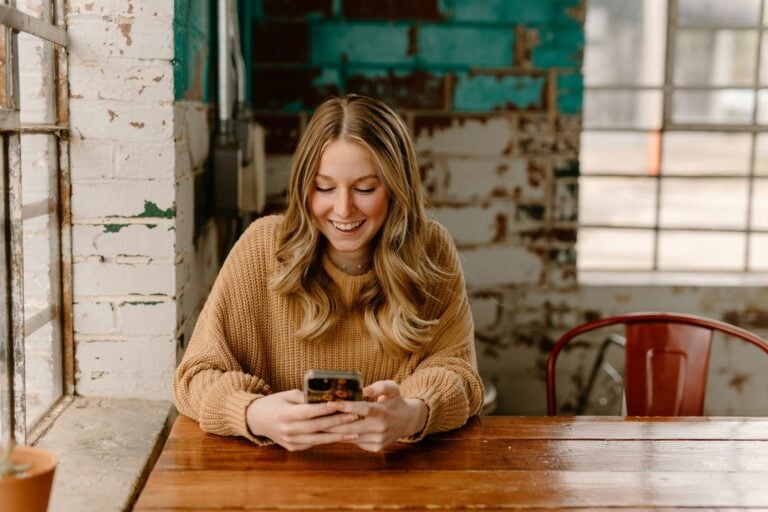A woman sitting at a table looking at her cell phone. Photo by Brooke Cagle, Unsplash