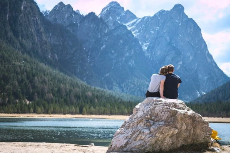 A couple sits on a rock looking out over a lake. Photo by Timo Stern, Unsplash