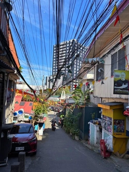 Overhead cables crisscross above a narrow street in Cebu City. Photo by Nikola Mikovic