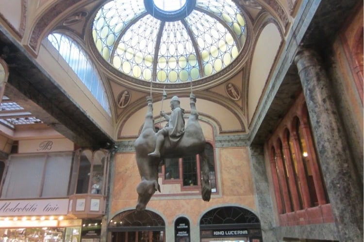 A life-sized horse hanging upside down, with Saint Wenceslas seated calmly beneath its belly in Lucerna Passage. Photo by Brent Cassie