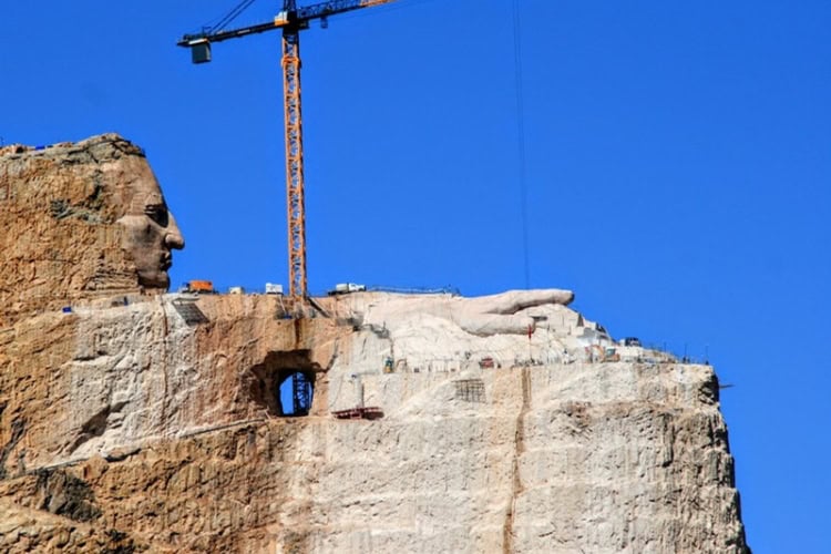 The Crazy Horse Memorial as seen in 2026, focusing on the arm and hand. A colossal high-top crane over 215 feet tall aids the carving process. Photo by Frank Hosek
