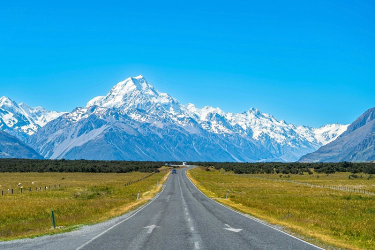 A road leads to snowy mountains under clear skies in Glentanner, New Zealand. Photo by JinHui CHEN, Unsplash