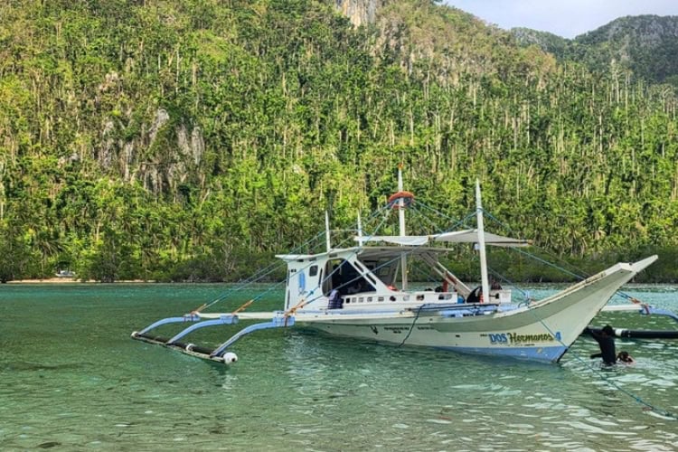 A Dos Hermanos island-hopping boat anchors near a forested shoreline in El Nido, Palawan, Philippines. Photo by Kurl Ivan I. Fernandez