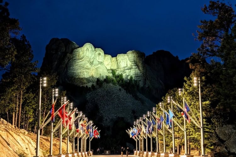 Mount Rushmore National Memorial at night. The Avenue of Flags features 56 flags representing all 50 states, one district, three territories, and two commonwealths of the United States. Photo by Frank Hosek