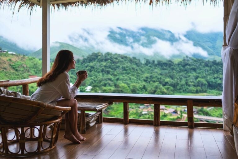 A woman drinks coffee and looks at mountains and green nature. Photo by Getty Images, Unsplash
