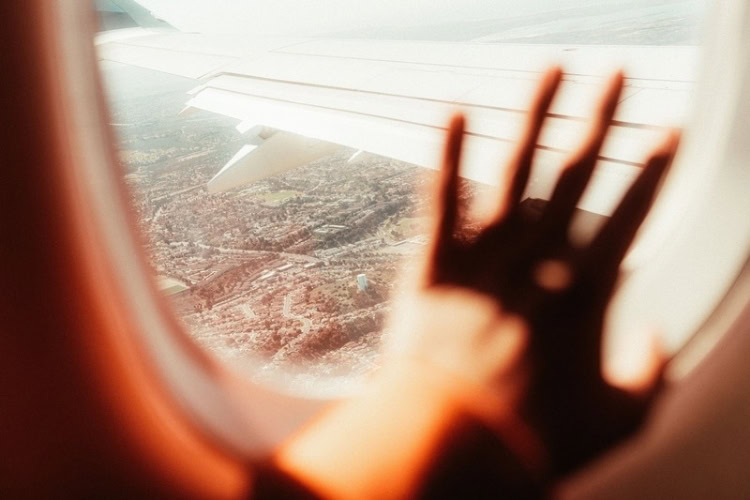 Scenic view from an airplane window with hand silhouette. Photo by Adrian Ozuna, Pexels