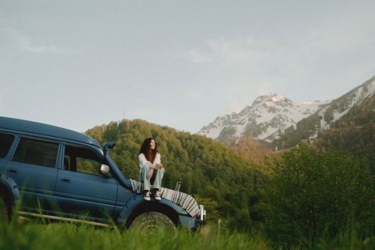 A woman sitting on an SUV with scenic mountain views. Photo by Anastasia Shuraeva, Pexels