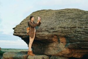 Young tourist woman backpacker on a large rock formation capturing the sunset landscape. Photo by Vitaly Gariev, Unsplash