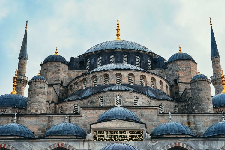 Stunning architectural detail of the Blue Mosque in Istanbul, showcasing its iconic domes and minarets under a cloudy sky. Photo by Ncang Jack, Pexels